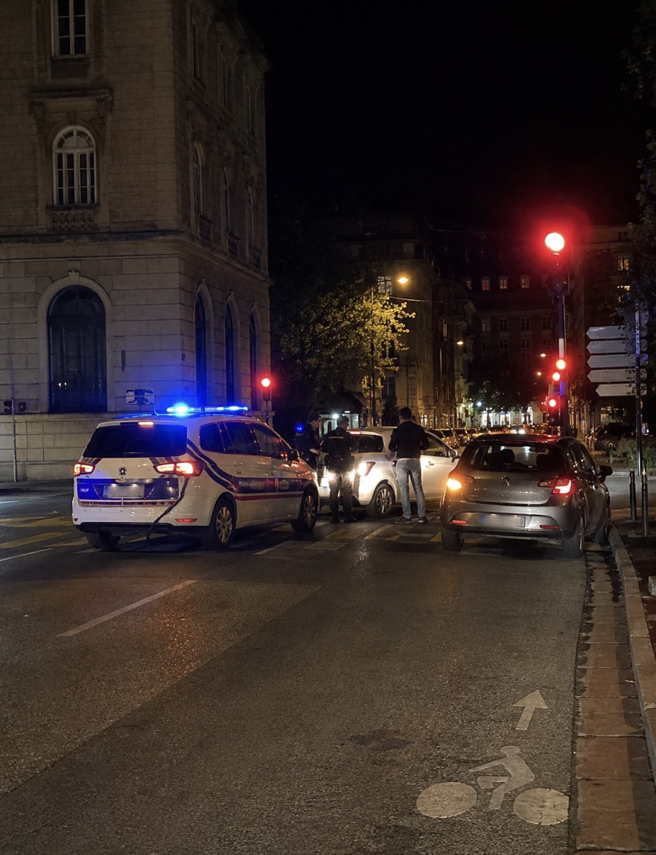 Voiture de police et véhicule arrêtés à une intersection de Grenoble de nuit, illustration contextuelle d’un accident après le franchissement d’un feu rouge.