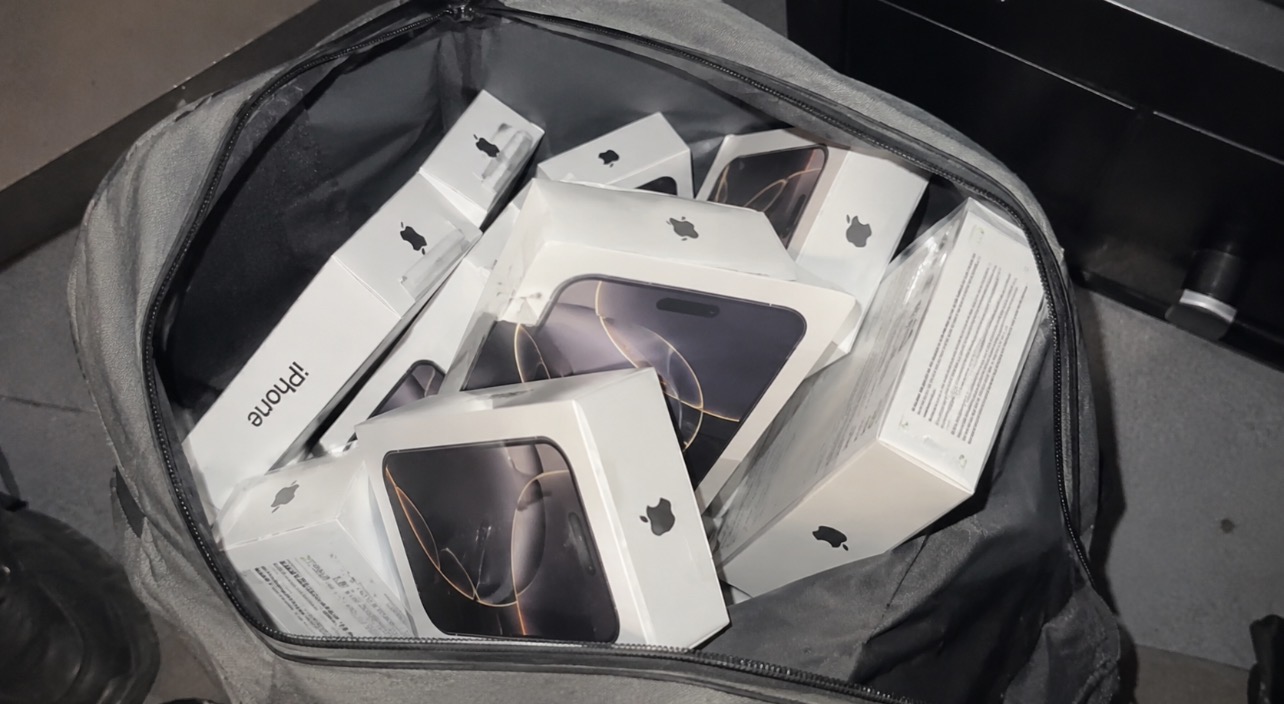 Sac gris ouvert rempli de plusieurs boîtes d’iPhone blanches, photographié en gros plan.