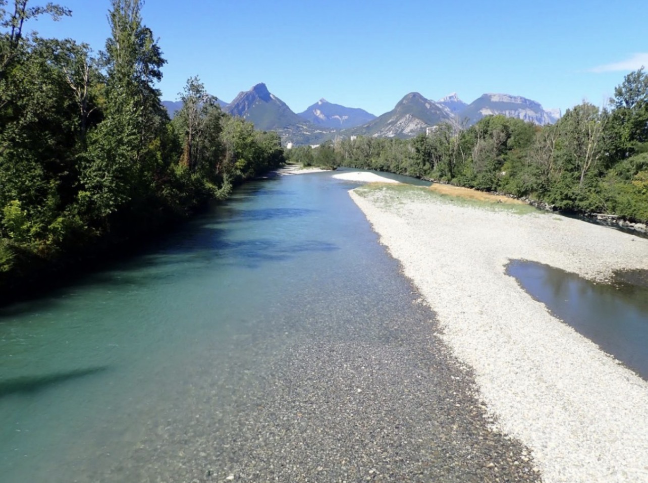 Le Drac traversant Grenoble avec les berges et la Bastille en arrière-plan.