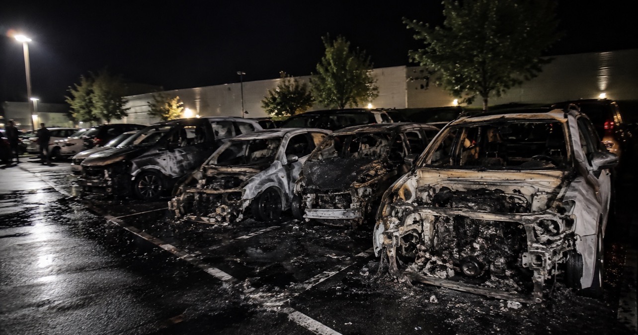 Parking de la gare de Gières avec plusieurs véhicules endommagés après un incendie nocturne.