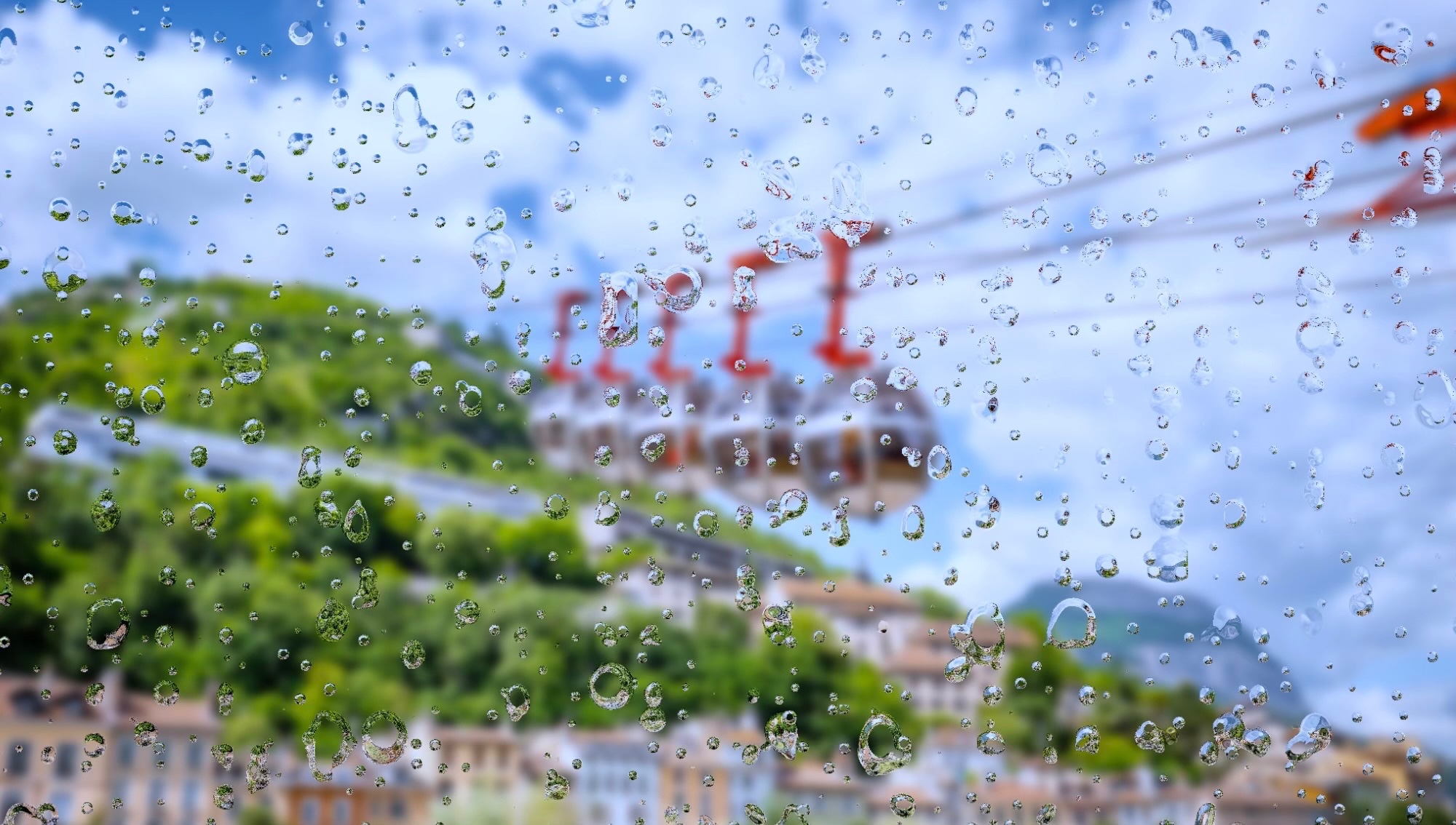 Vue de Grenoble sous la pluie en automne, avec les immeubles de la ville, les rues mouillées et les montagnes partiellement cachées par les nuages, pour illustrer sa troisième place au classement des villes françaises les plus pluvieuses.